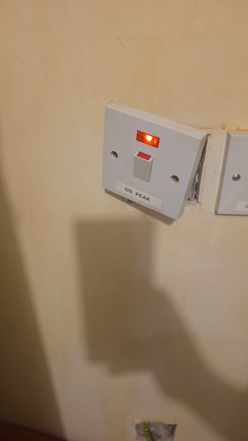 White electrical switch labeled 'ON PEAK' with a red indicator light illuminated on a beige wall.