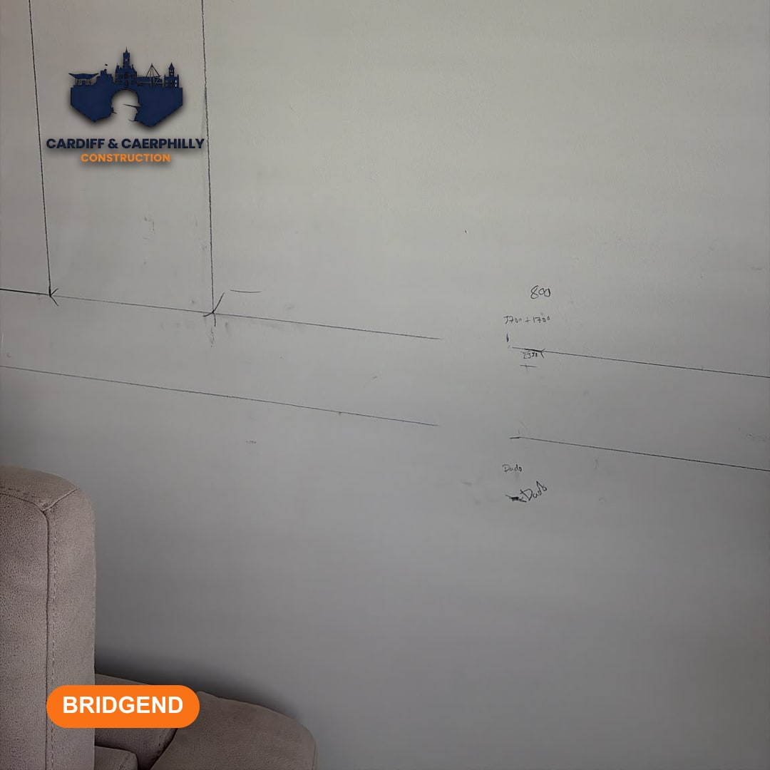 Pencil lines and measurements drawn on a light-coloured wall, showing layout planning, with a corner of a sofa visible.