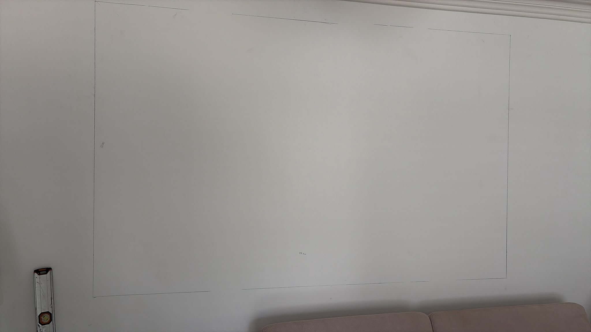 White wall with precise pencil markings outlining an area for installation, with a spirit level positioned at the left.