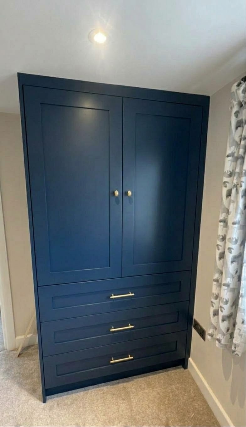 Dark blue fitted wardrobe with two upper doors and three lower drawers, featuring brass bar and knob handles, on a carpeted floor.