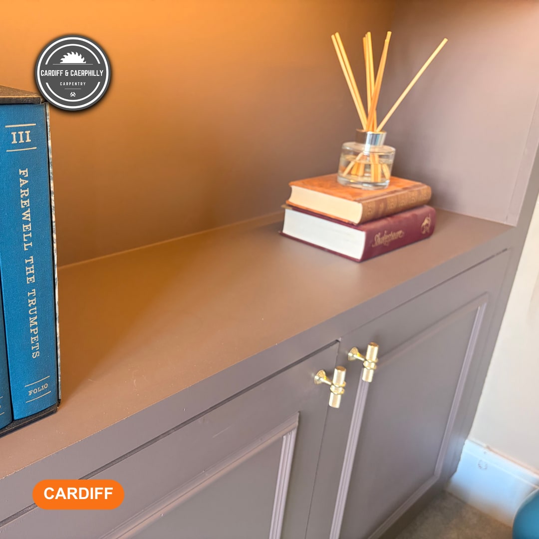 Close-up of a finished built-in wooden cabinet painted a dark taupe, featuring books and a reed diffuser on the shelf.