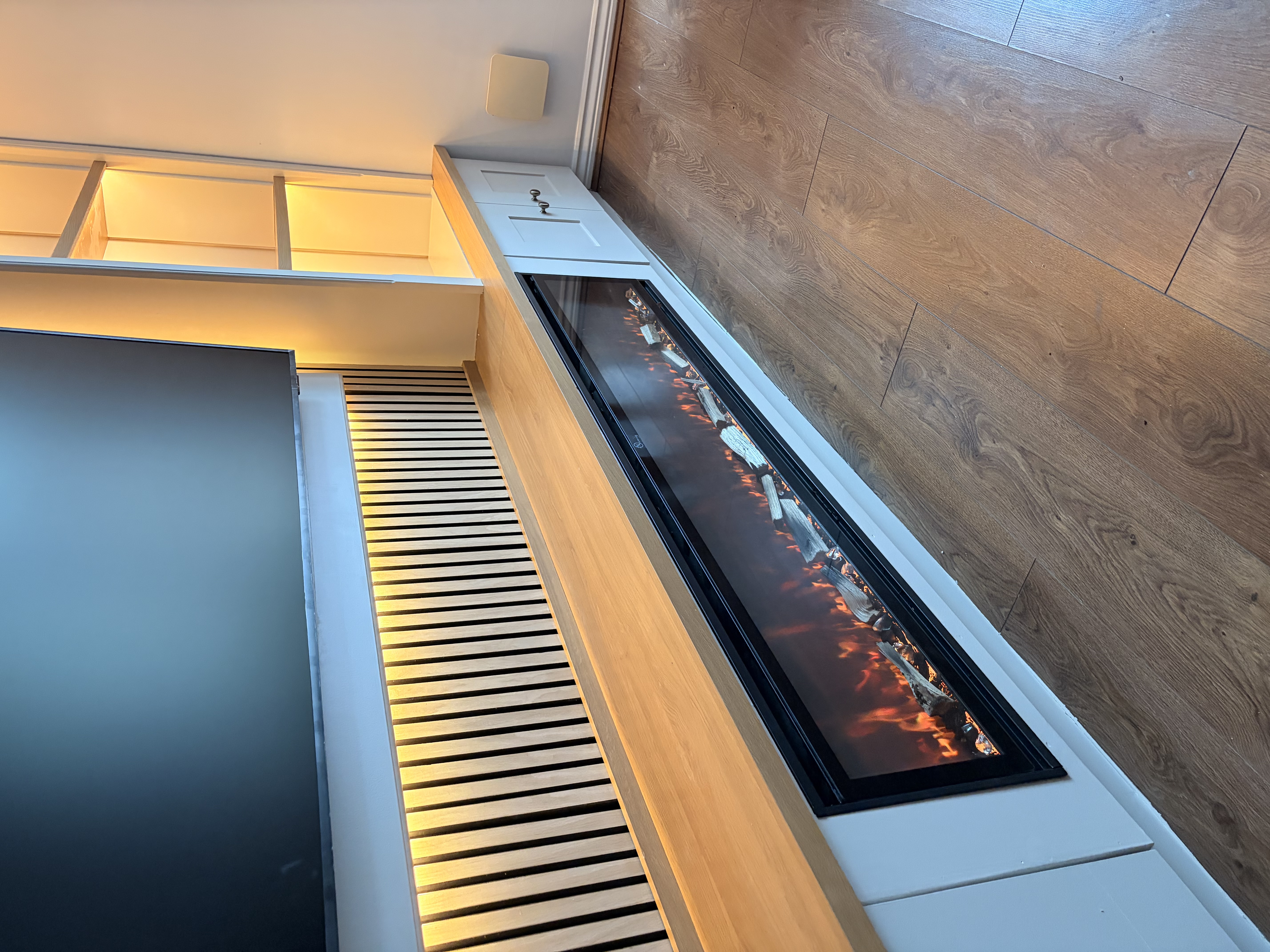 Custom built-in media unit with an integrated electric fireplace, slatted wood paneling, accent lighting, and shelving.