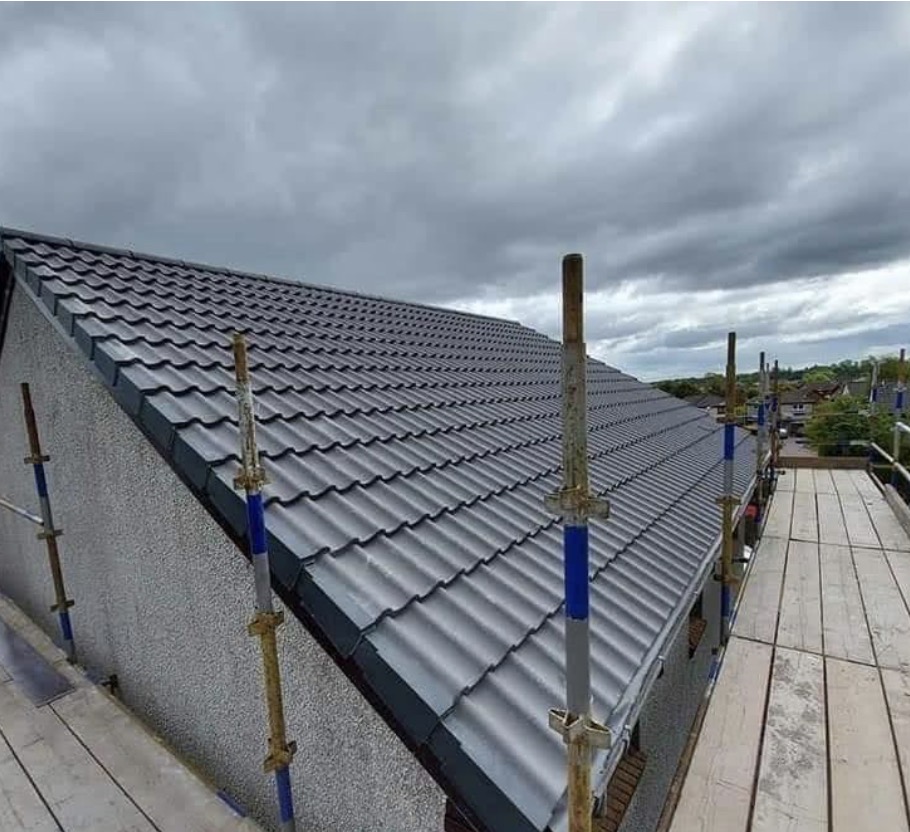 Newly installed grey tile roof on a house, with scaffolding visible on a cloudy day.