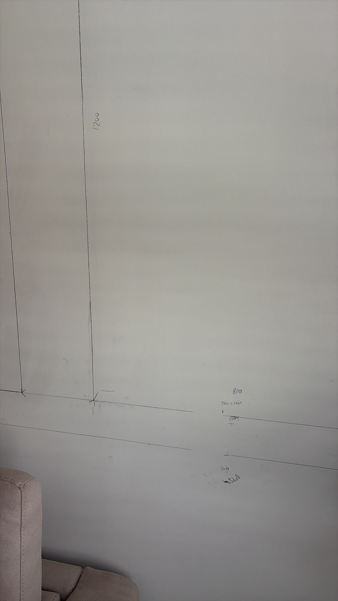Pencil lines and measurements drawn on a light-coloured wall, showing layout planning, with a corner of a sofa visible.