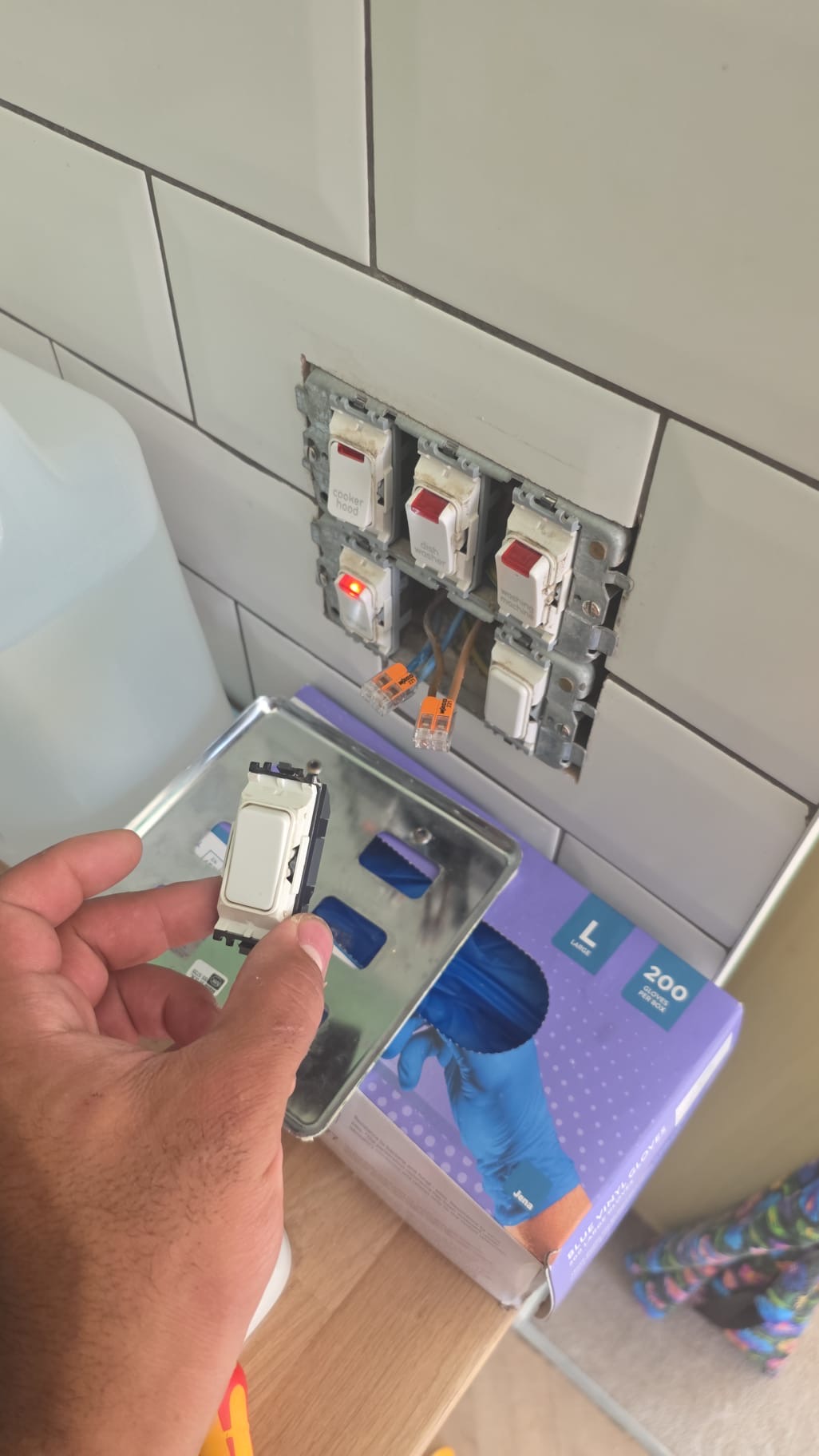 Electrician's hand holding a white electrical switch module during installation into a multi-gang faceplate on a tiled wall.