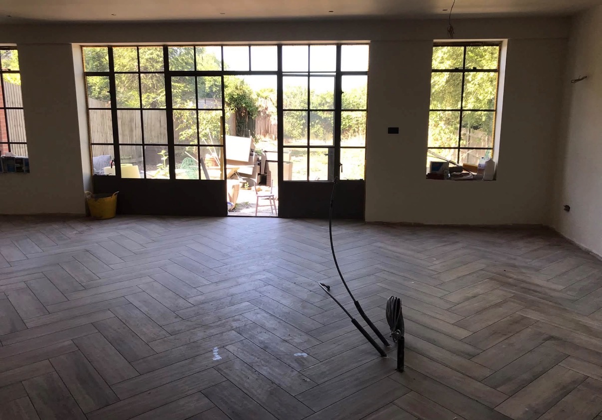 New herringbone wood flooring in a bright room with large black-framed windows and patio doors.