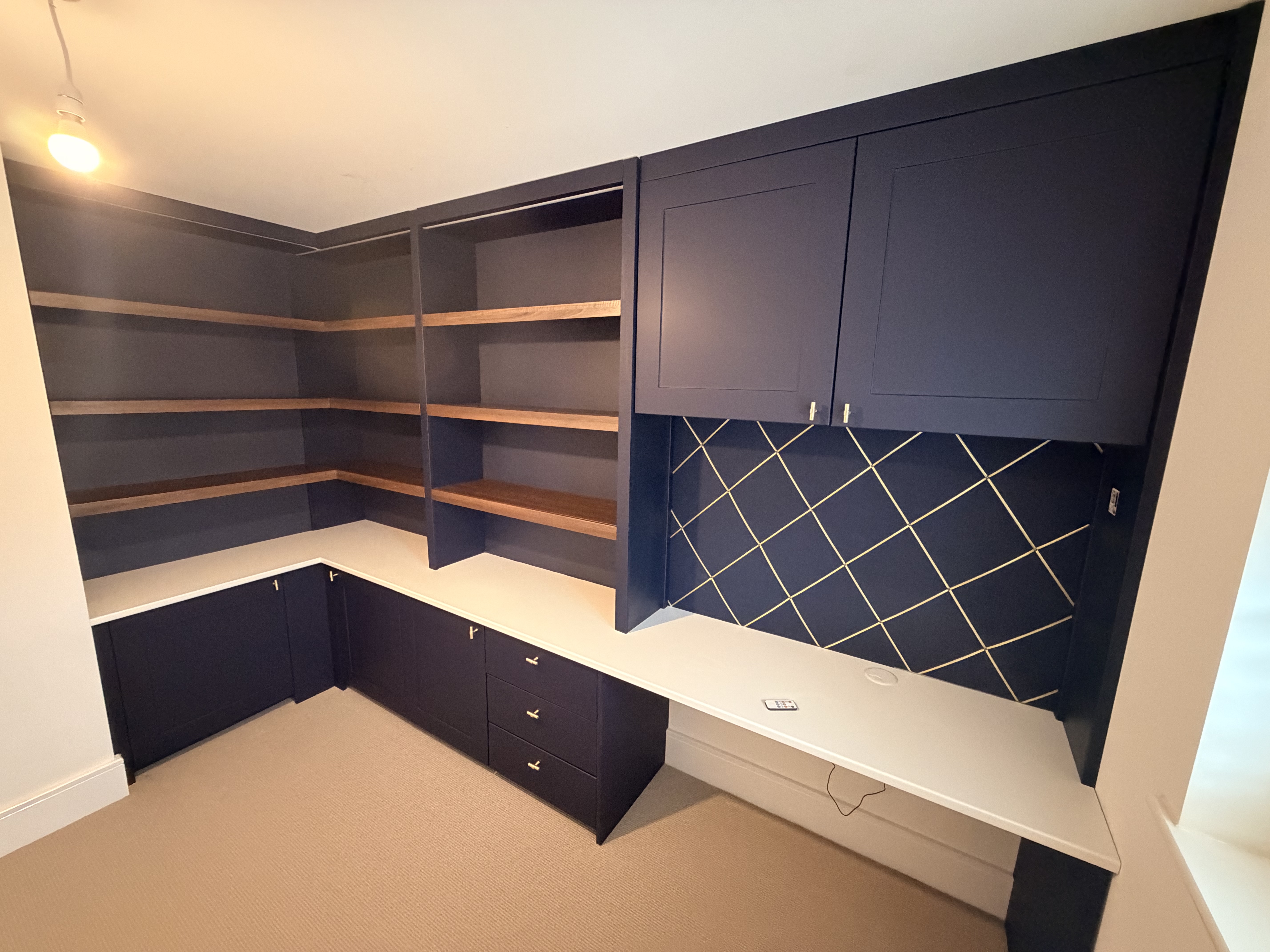 Custom dark blue fitted home office furniture with light wooden shelves, white countertops, and an integrated desk.