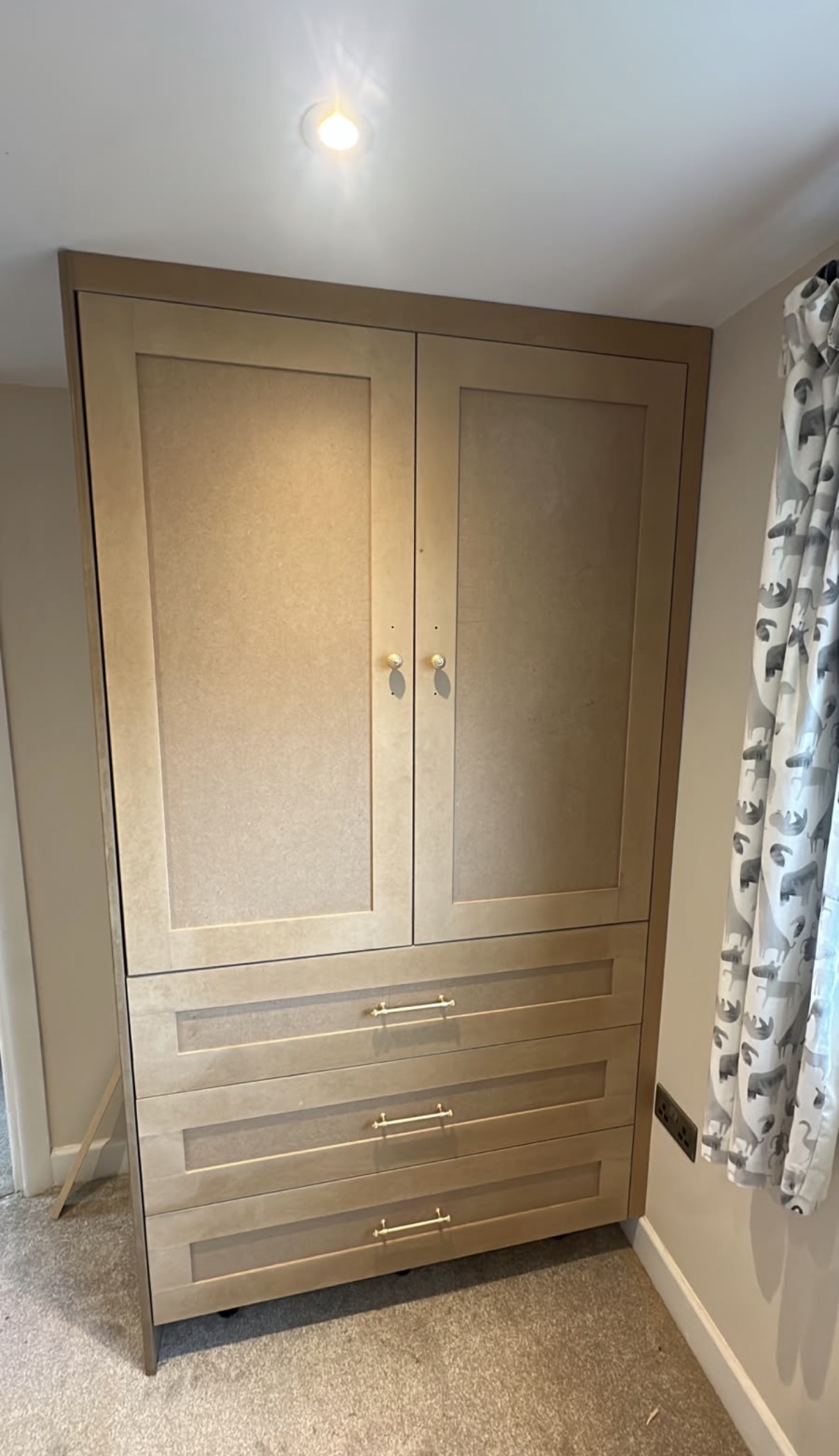 Custom-built fitted wardrobe made from raw MDF, featuring two cabinet doors and three drawers with brass handles.
