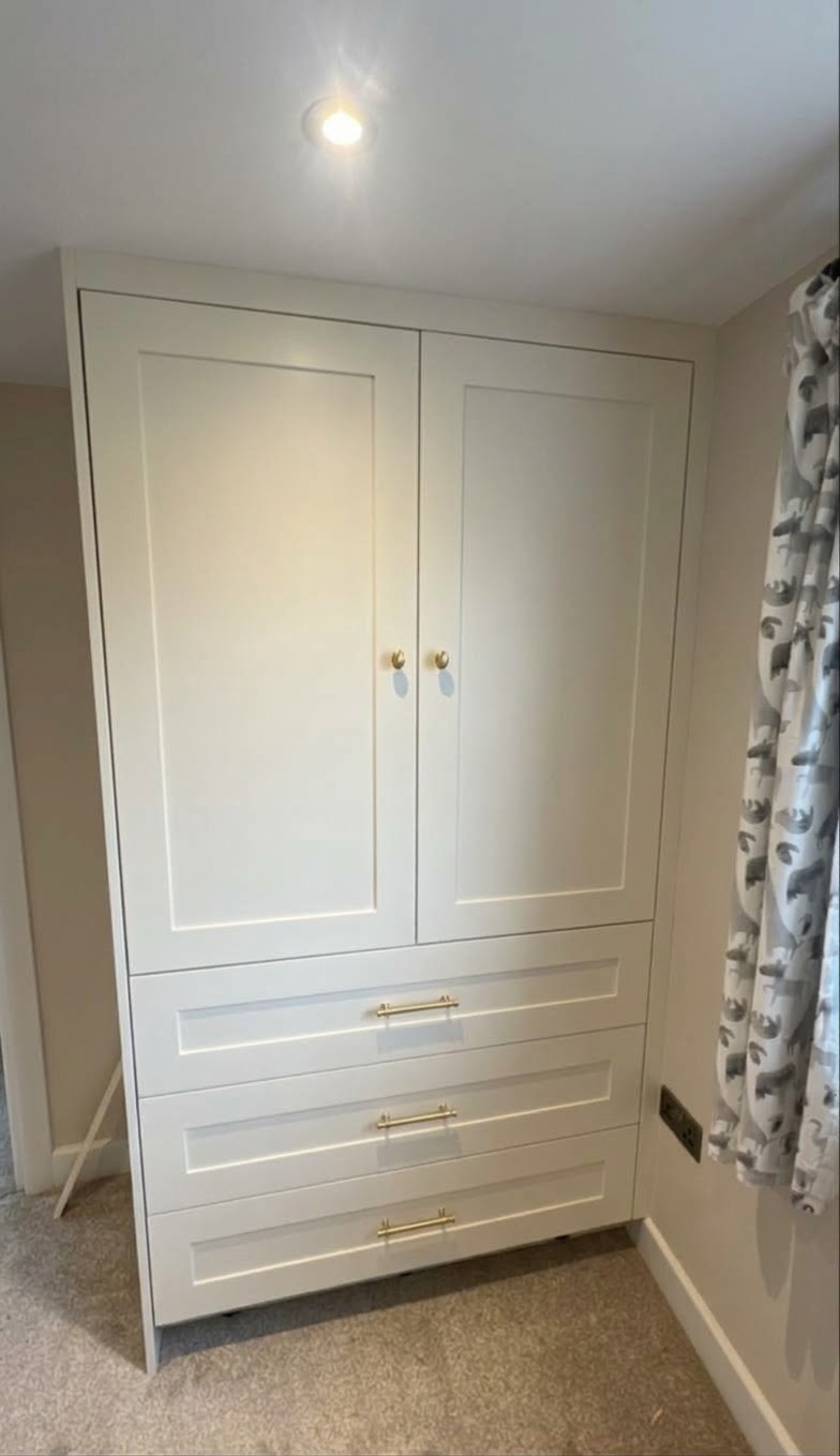White fitted wardrobe with gold handles, four cabinet doors, and three drawers, installed in a carpeted bedroom.