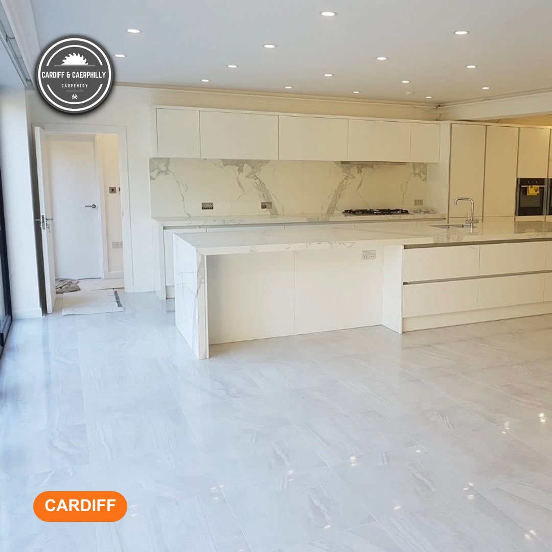 A spacious modern white kitchen featuring a large island, marble-effect countertops and splashback, integrated appliances, and light grey tiled flooring.