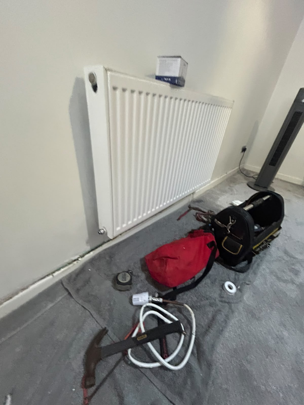 White panel radiator installed on a wall with plumbing and heating tools on a protective sheet during a work in progress.