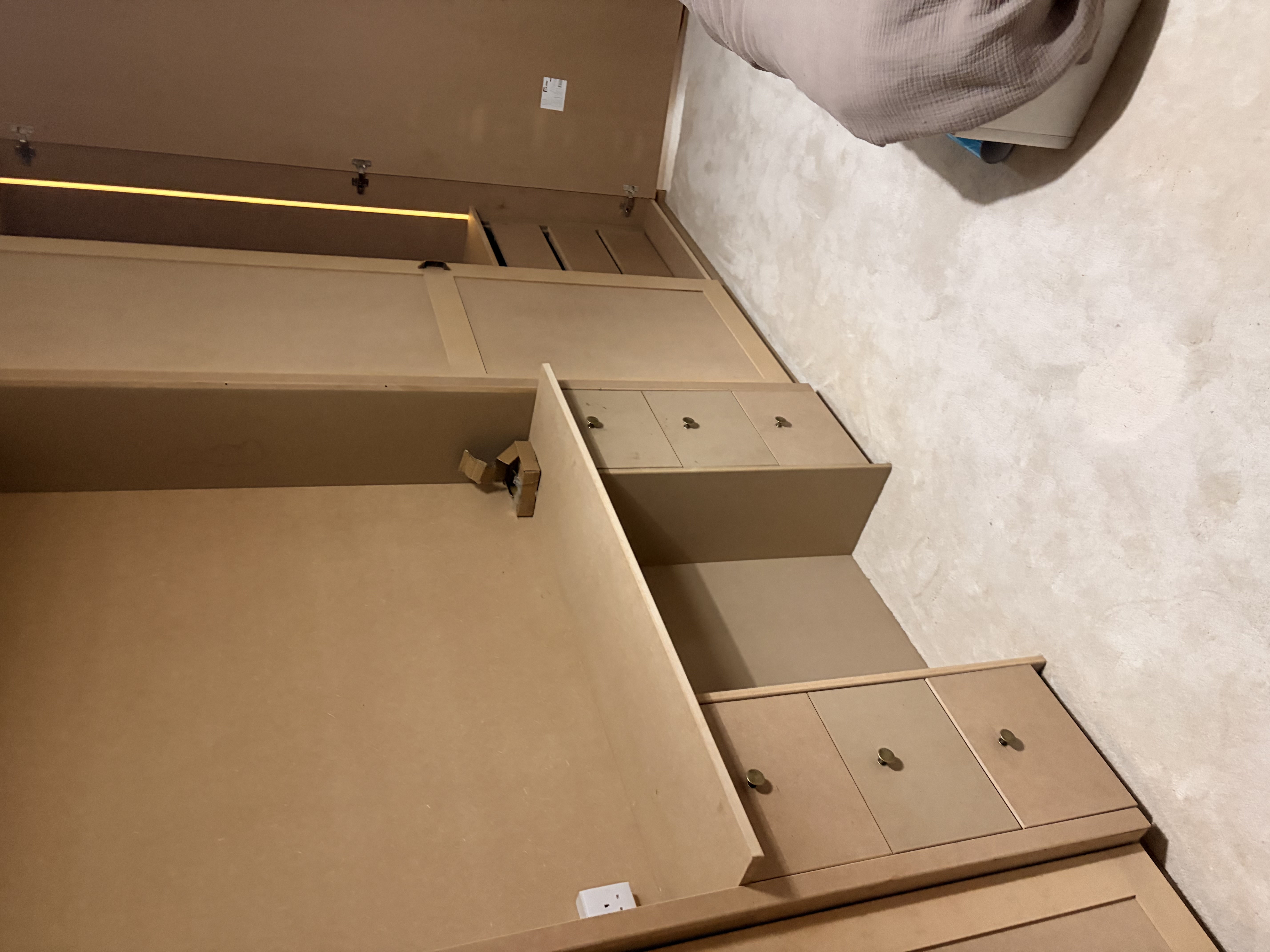 Unpainted bespoke fitted carpentry, including a desk with drawers and wardrobes in a bedroom, ready for finishing.