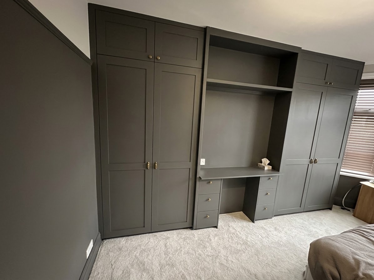 Dark grey fitted wardrobe and integrated desk unit in a modern bedroom, showcasing bespoke carpentry work and storage.