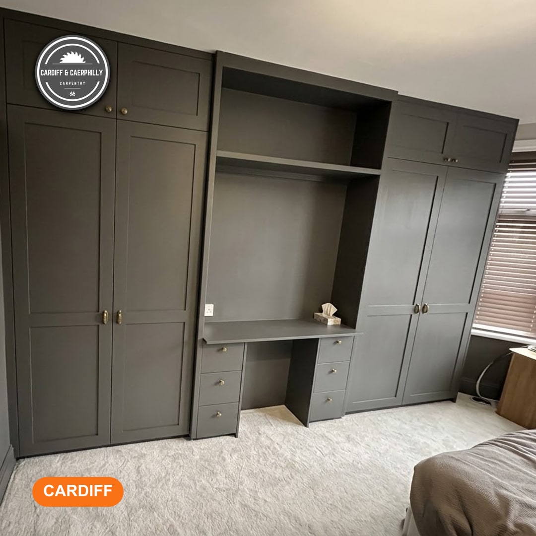 Modern dark grey fitted wardrobes and integrated desk unit in a bedroom with a light grey carpet and window blinds.