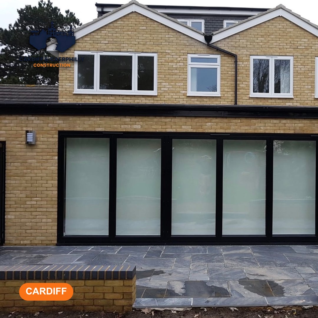Modern house extension featuring large black bi-fold doors, new light yellow brickwork, white windows upstairs, and a dark paved patio.