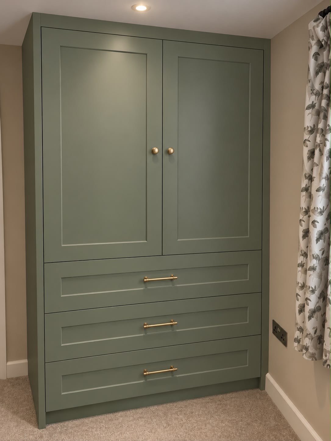 Fitted green wardrobe with gold handles, built-in to a bedroom, providing custom storage solution.