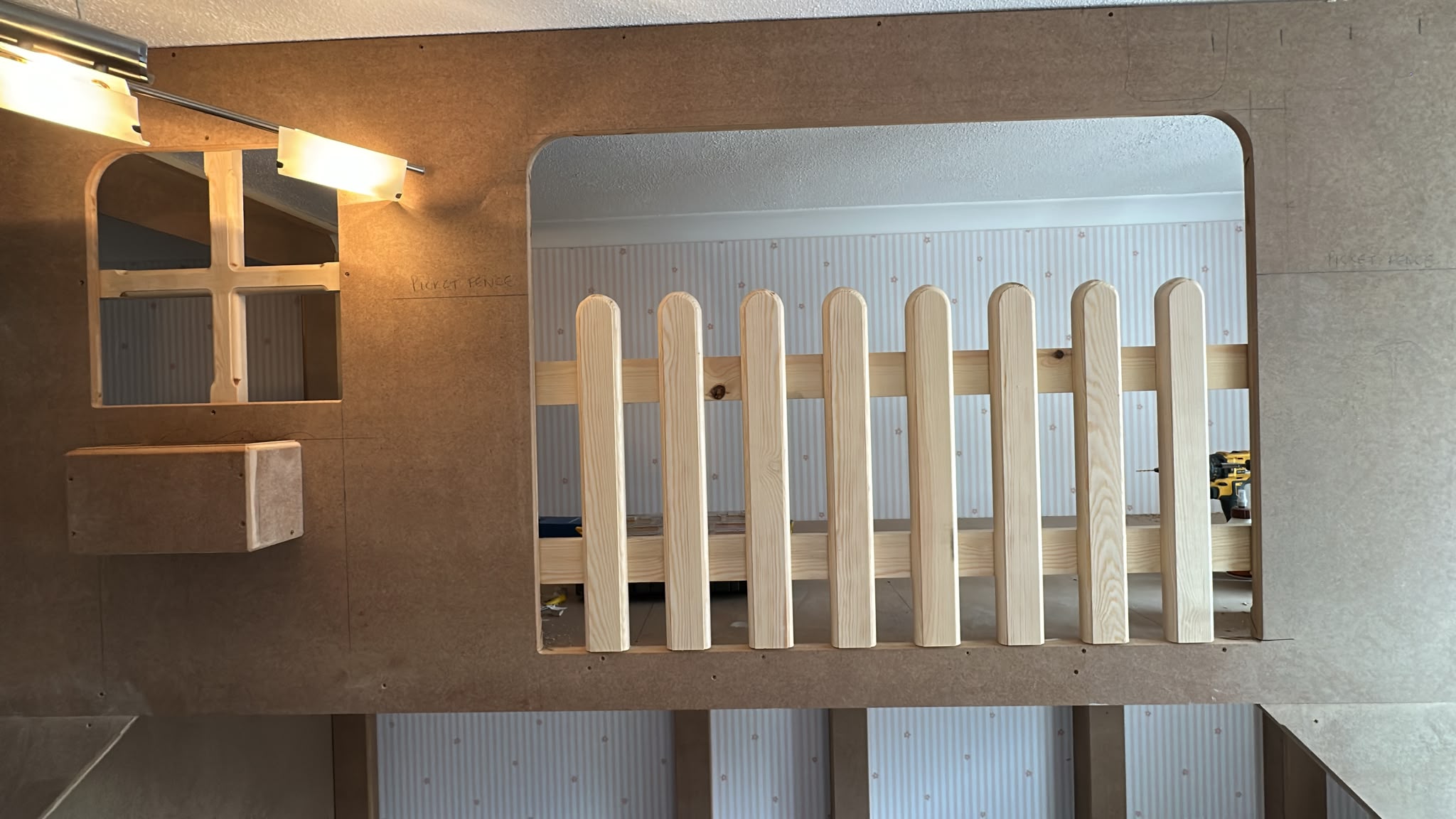 Close-up of a custom MDF and wood playhouse structure under construction, featuring a window and picket fence railing.