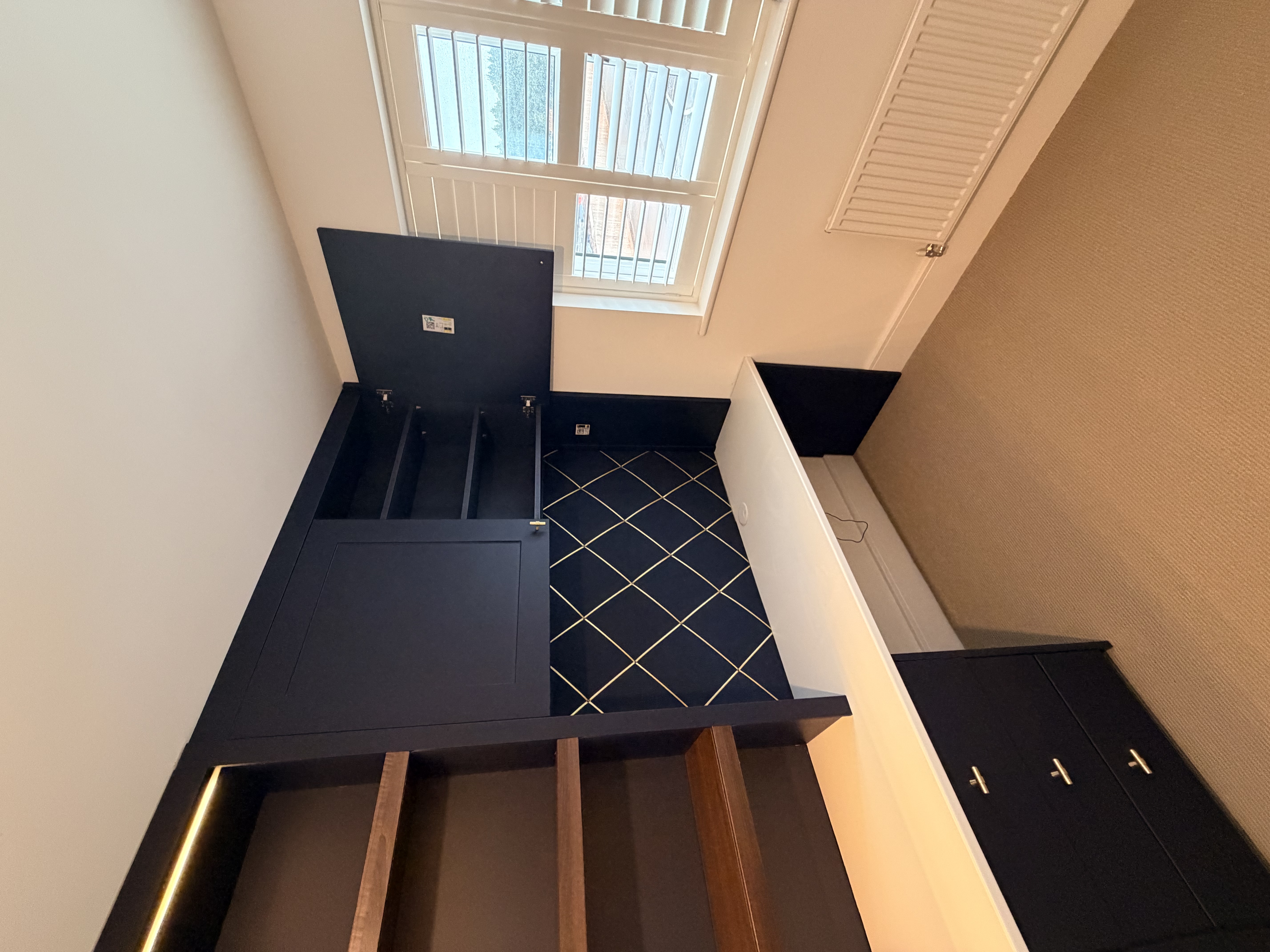 Custom dark blue fitted home office unit with a white desk, wooden shelves, and integrated lighting in a modern room.