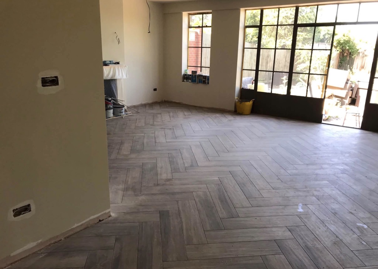 Light grey herringbone floor in a spacious room with large industrial-style windows, walls partially ready for finishing.