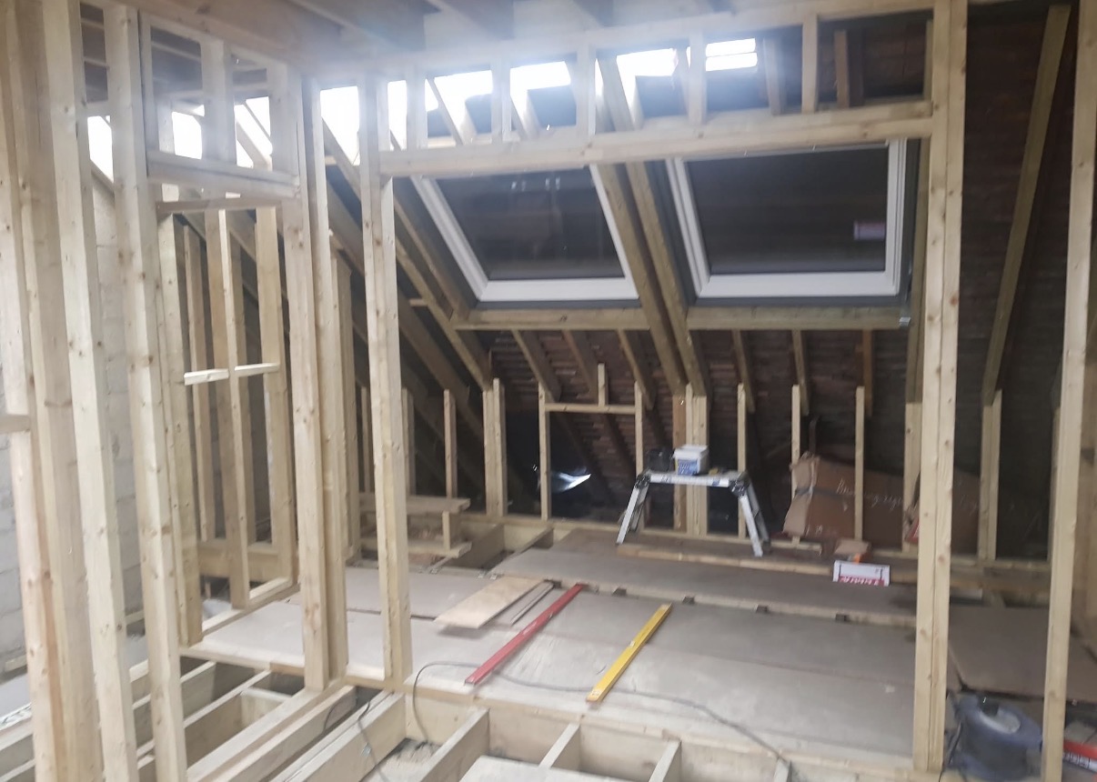 Interior view of a loft conversion in progress, showing new timber wall and roof framing with two installed skylight windows.