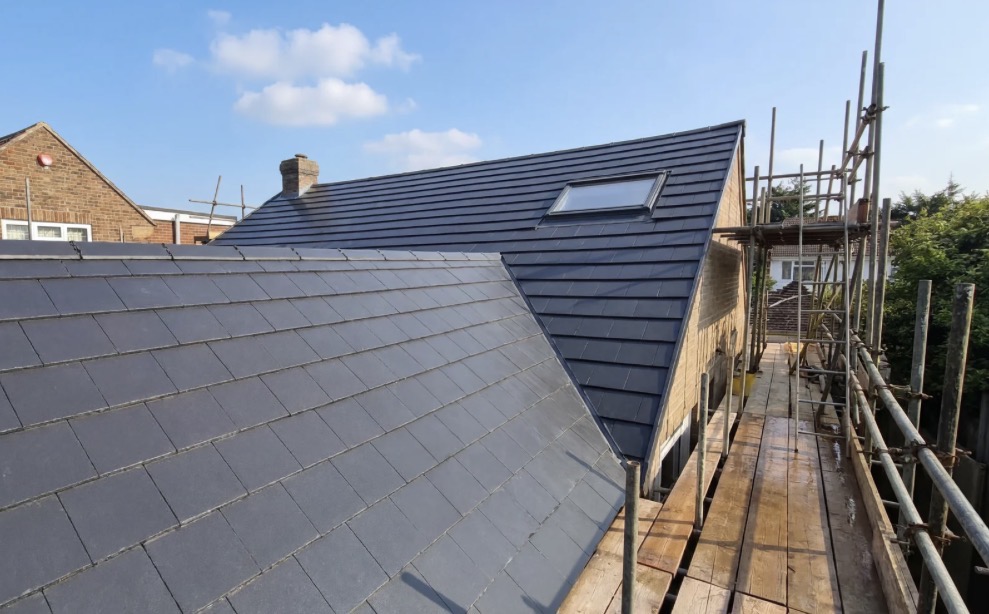 Newly installed dark grey roof tiles on a residential property featuring a modern skylight and surrounding scaffolding.