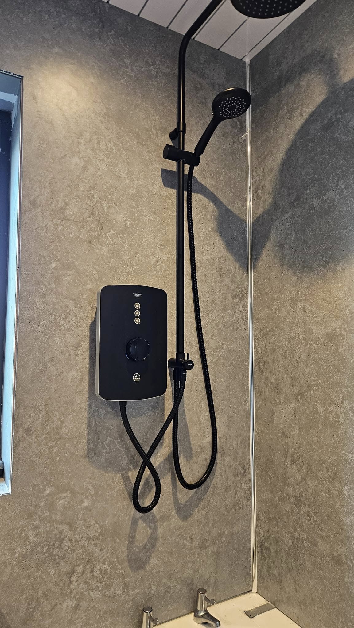 Modern black electric shower unit and matching shower head installed on grey textured wall panels in a contemporary bathroom.