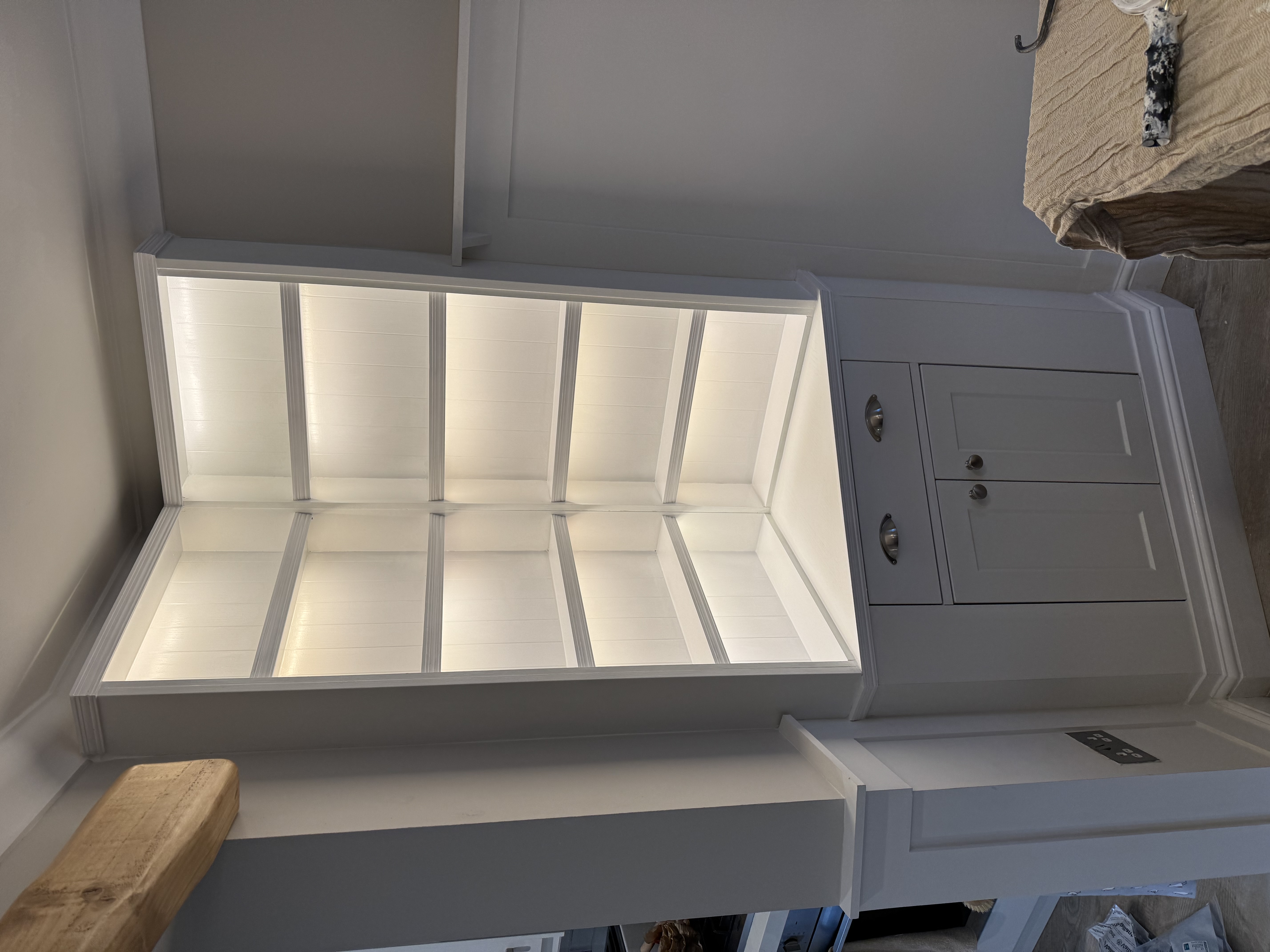 White bespoke fitted corner cabinet with integrated LED shelf lighting, lower drawers, and cupboards, showcasing custom carpentry work.