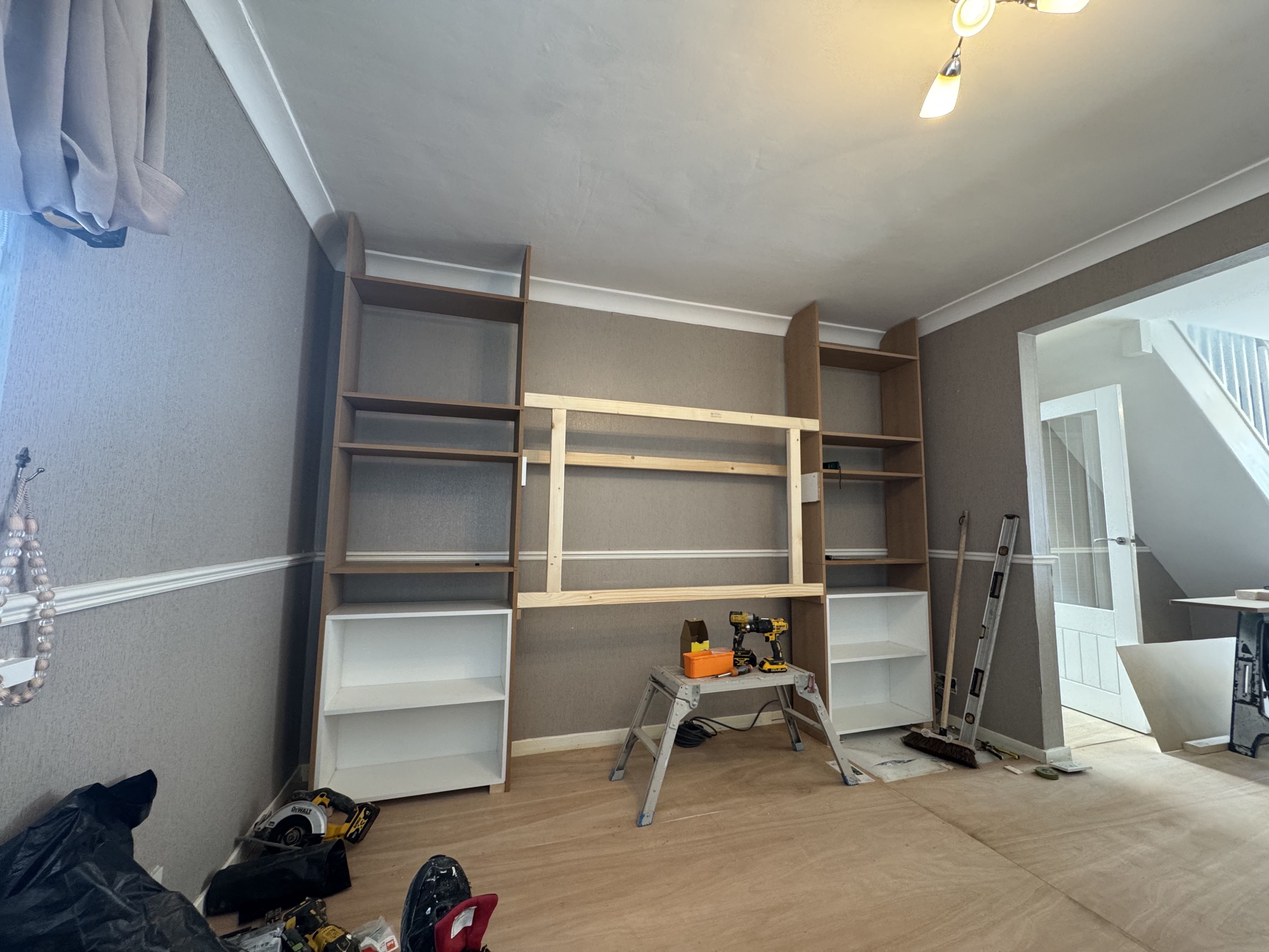 Custom carpentry in progress, featuring fitted wooden shelving units and a media frame in a living room renovation.